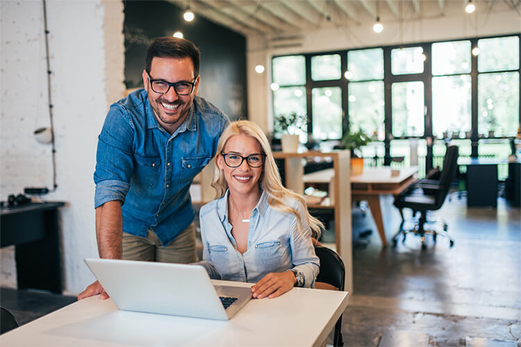 Cheerful female entrepreneurs smiling at the camera while working in their ceramic store. Happy young ceramists using a laptop together. Two young businesswomen running a successful small business.